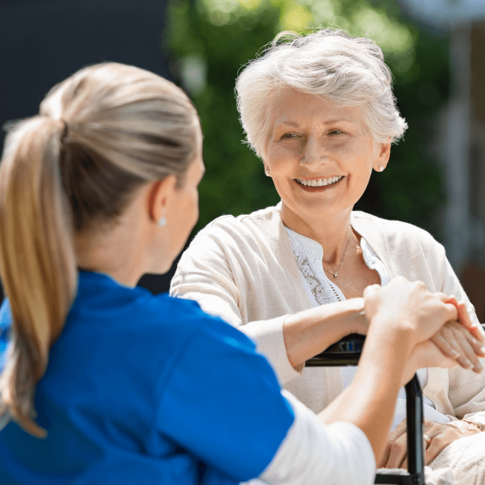 Caregiver holding hands with a smiling elderly woman outdoors